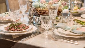 Una mesa de comedor dispuesta con cristalería, platos y velas, con un centro de huevos de Pascua y follaje.