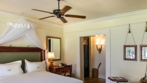 Habitación de hotel con una cama grande, un escritorio, una silla, un ventilador de techo y una puerta que da a otra habitación.