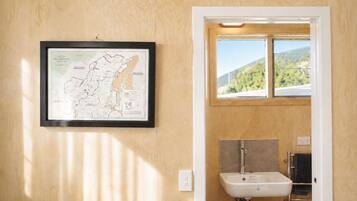 Une carte encadrée du parc national du mont Aspiring est accrochée à un mur en bois, une fenêtre offre une vue sur la verdure, et la salle de bain est équipée d’un lavabo et d’un porte-serviettes.
