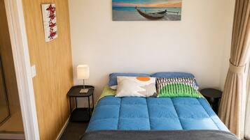 Une chambre d’hôtel avec un lit, une table de chevet avec une lampe, un tableau représentant un bateau accroché au mur et une vue sur la mer.