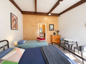 Een kamer met twee bedden, een tafeltje, een stoel, een kapstok en een spiegel.