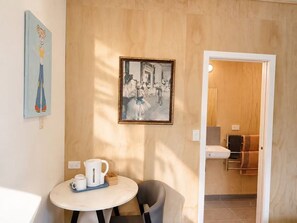 Een kamer met een ronde tafel, een stoel, een schilderij en een deur naar een badkamer.