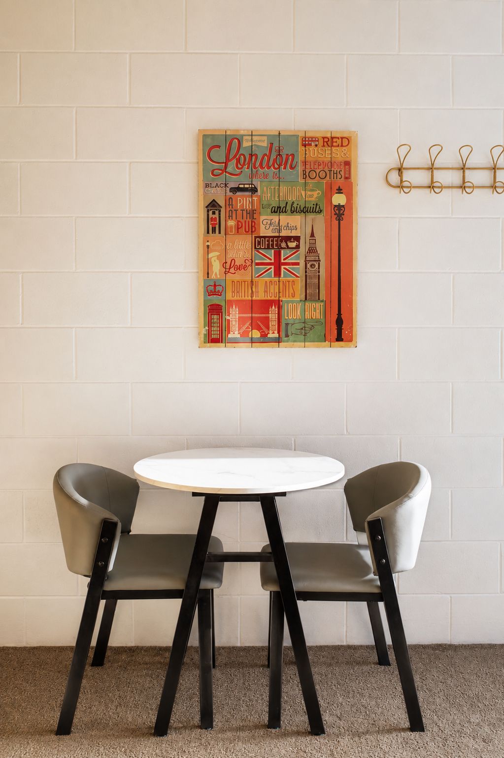 Una habitación con una mesa redonda y dos sillas, una obra de arte colgada en la pared que muestra monumentos de Londres, y un perchero con ganchos.