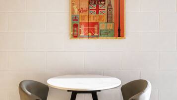 A room with a round table and two chairs, a wall-mounted artwork depicting London landmarks, and a coat rack with hooks.