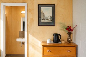 A bathroom with a wooden vanity, a framed picture on the wall, and a vase with flowers.