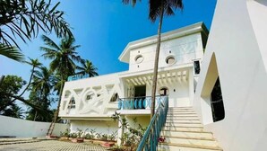 Un bâtiment blanc avec un escalier menant à un balcon, entouré de palmiers.