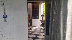 Ein Zimmer mit Schachbrettmuster, einem Holztisch mit einer Flasche und einem roten Gegenstand, sowie ein Durchgang zu einem weiteren Raum mit einem Stuhl und einem Tisch.