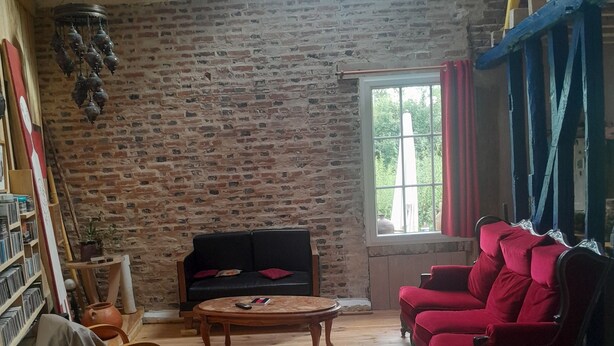 Ein Zimmer mit Backsteinwand, Holzboden, einer Couch, roten Stühlen, einem Tisch und einem Deckenventilator.