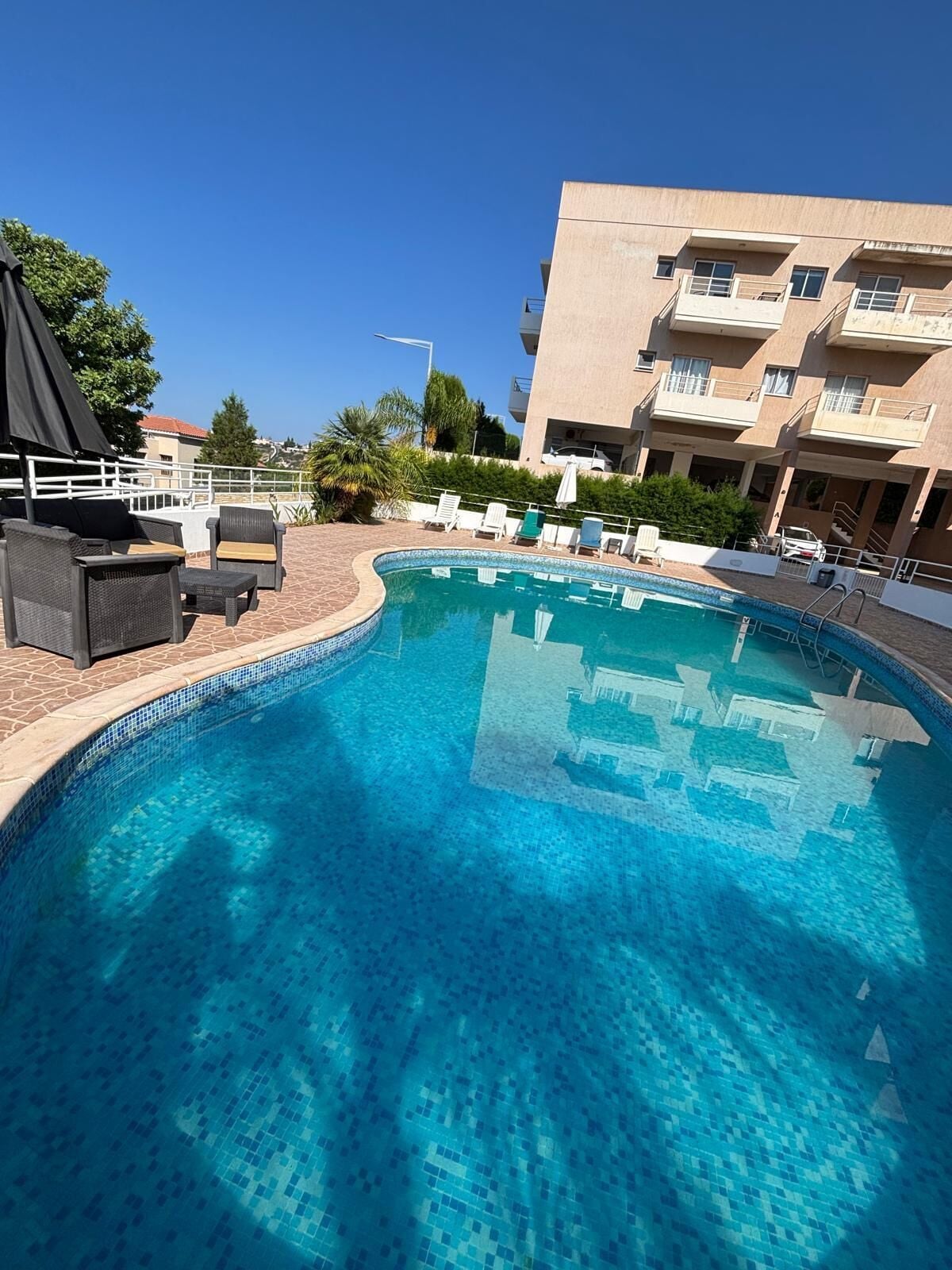 A swimming pool with lounge chairs and umbrellas, surrounded by a building with balconies.