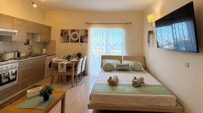 Ein kompaktes Hotelzimmer mit einer Küchenzeile, einer Essecke, einem Bett mit aufgerollten Handtüchern und einem großen Fenster mit Blick.