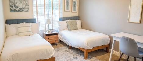 A bedroom with two beds, a desk, and a chair.