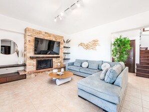 A modern living room with a stone fireplace, a grey sofa, a coffee table, and a staircase leading to another level. - Leyland by Interhome (Faliraki)