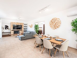 A modern living space with a dining area, a sofa, a TV mounted on a stone wall, and a decorative wall piece. - Leyland by Interhome (Faliraki)