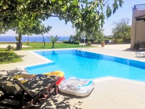 A swimming pool with a clear view of the ocean, surrounded by a patio area with lounge chairs and a table. - Leyland by Interhome (Faliraki)