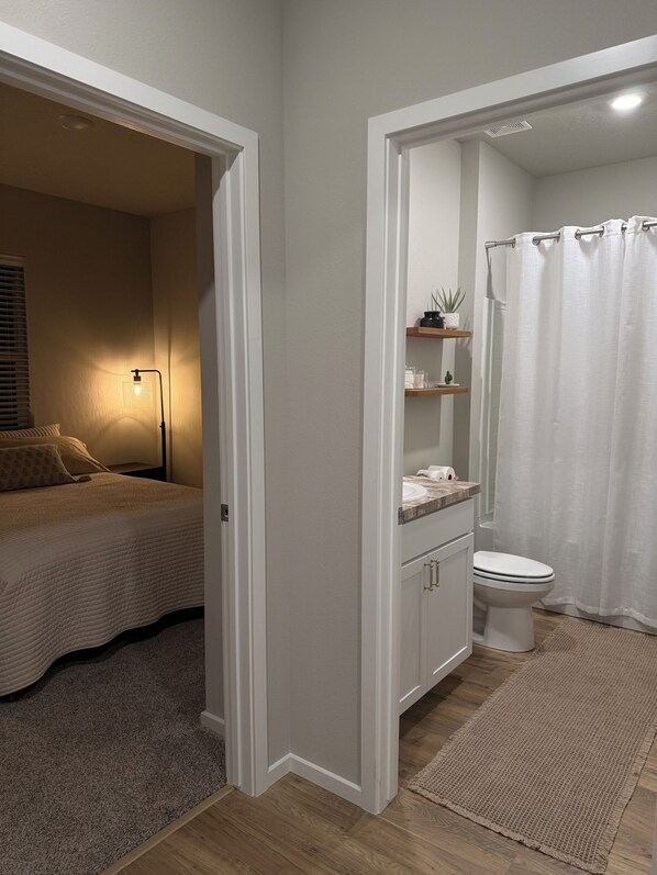 Ein Schlafzimmer mit Bett, Nachttischlampe und Nachttisch. Es gibt ein Badezimmer mit Toilette, Waschbecken und Duschvorhang.
