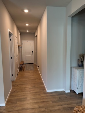 A hallway with wooden flooring, white walls, and a white door at the end. - BRAND NEW Cozy & Chic 3BR Retreat, Fireplace, EV Charger -Hearth & Home by Bree (Spokane Valley)