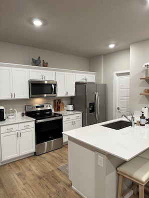 A modern kitchen with white cabinetry, stainless steel appliances, and a central island with a sink. - BRAND NEW Cozy & Chic 3BR Retreat, Fireplace, EV Charger -Hearth & Home by Bree (Spokane Valley)
