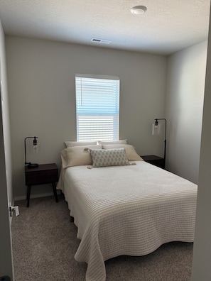 A bedroom with a bed, two bedside tables, a window with blinds, and a ceiling vent. - BRAND NEW Cozy & Chic 3BR Retreat, Fireplace, EV Charger -Hearth & Home by Bree (Spokane Valley)