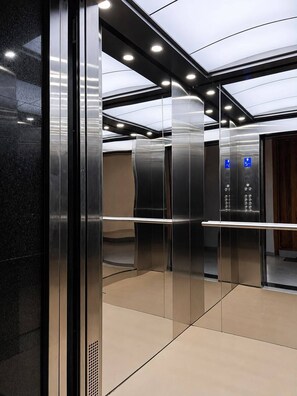 A modern elevator interior with reflective surfaces and a control panel displaying floor numbers. - Beach Apartment - right on the Beach! (with full Air Conditioning, Gym) (Mombasa)