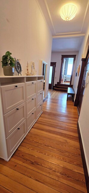 Ein Flur mit Holzboden, einer weißen Kommode mit Schubladen, einem Blumentopf und einem Schiffsmodell auf der Kommode.