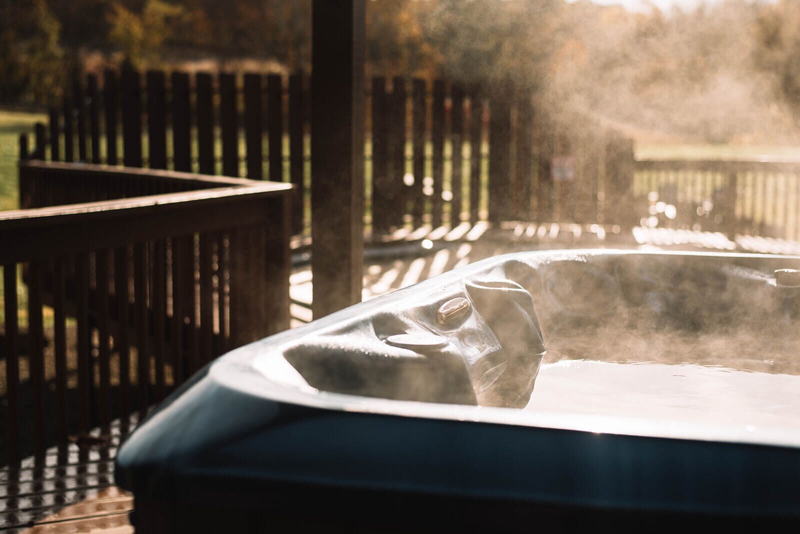 A hot tub with steam rising from it, surrounded by a wooden deck and a fence.