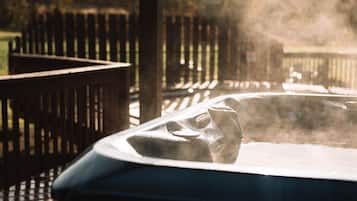 A hot tub with steam rising from it, surrounded by a wooden deck and a fence.