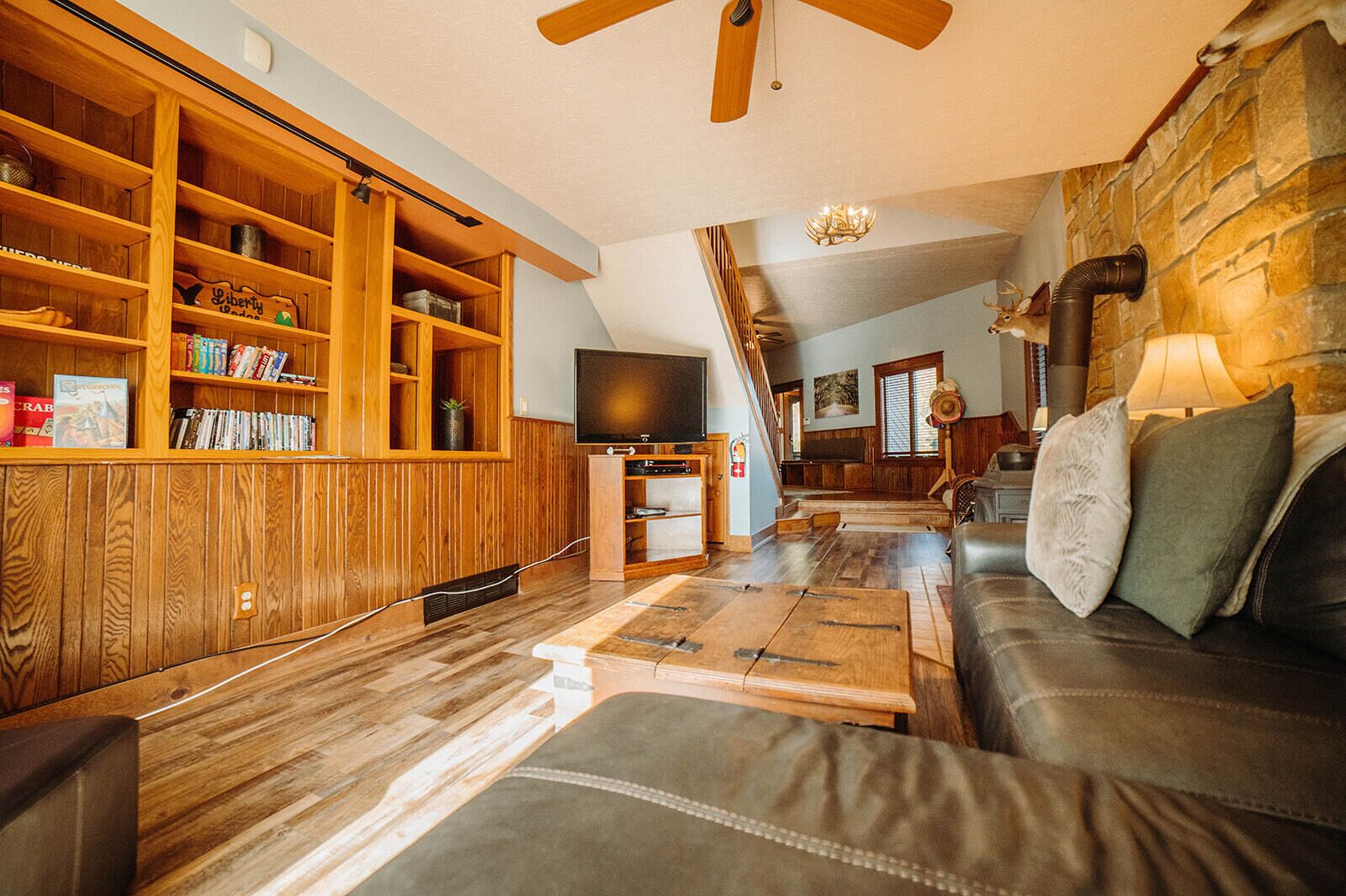 A cozy living room with a wooden bookshelf, a leather sofa, and a flat-screen TV.