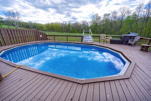 Ein rechteckiger Pool mit Holzterrasse, umgeben von einem Holenzaun, und einem Sitzbereich mit Stühlen.