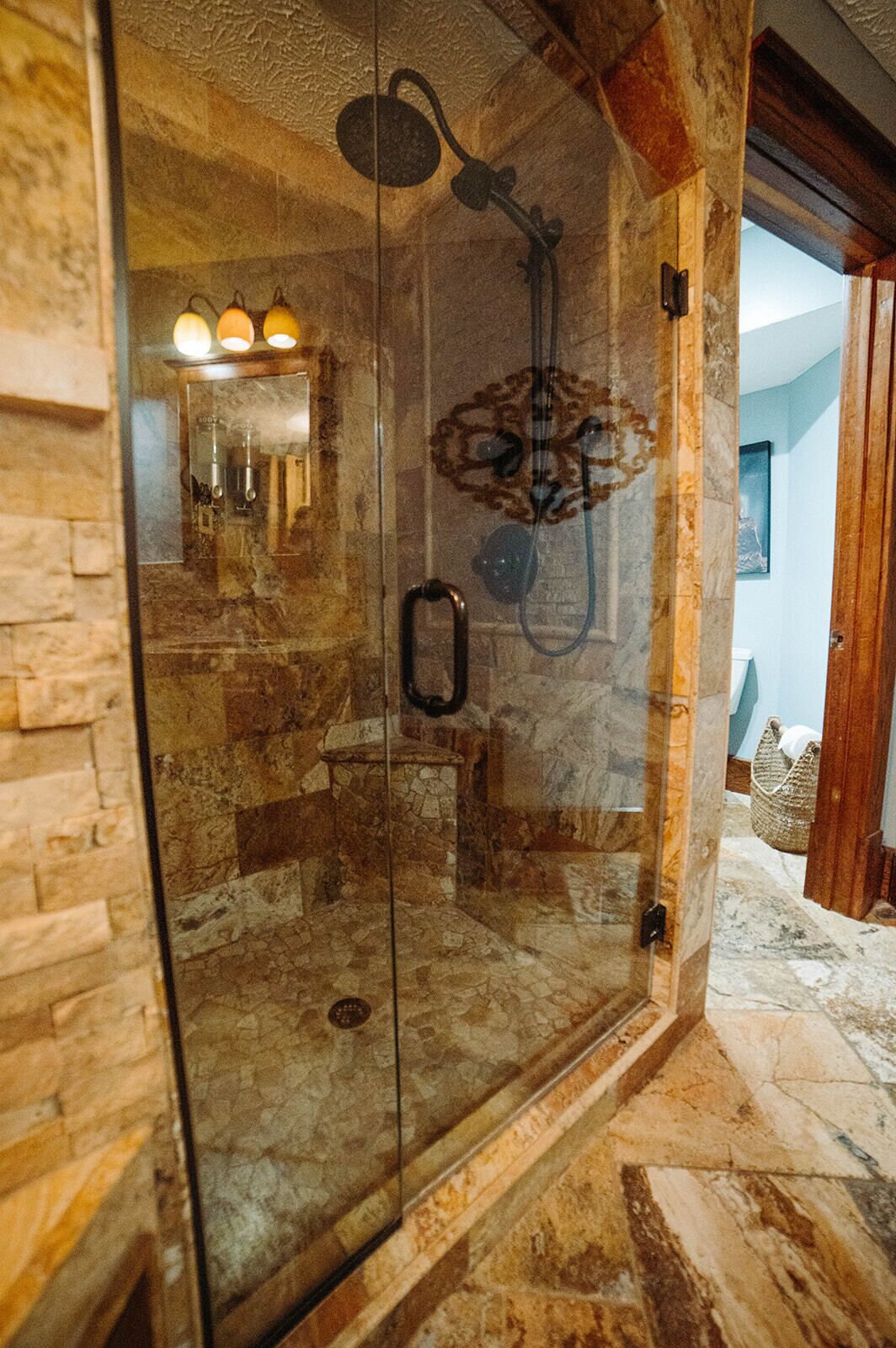 A glass-enclosed shower with a stone wall backdrop, a handheld showerhead, and a glass door with a handle.