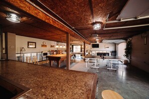 Un grand espace intérieur comprenant une table de billard, un bar et un coin salon offrant une vue sur l’extérieur.