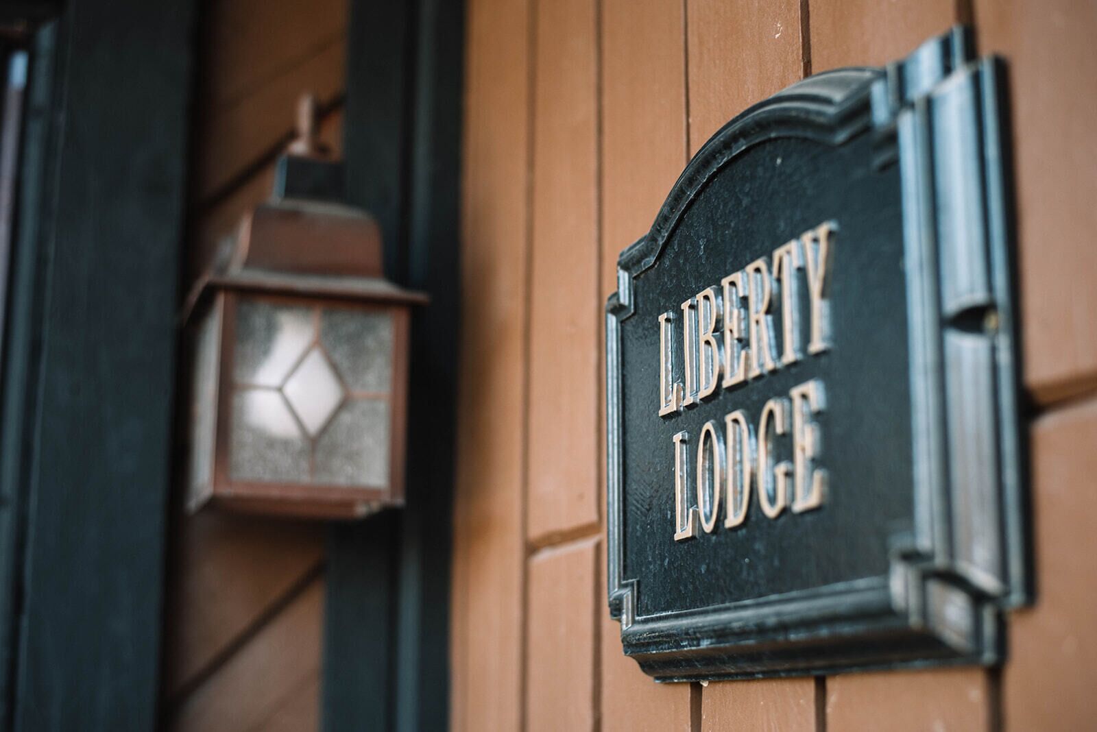 Uma placa preta com a inscrição 'LIBERTY LODGE' fixada em uma parede de madeira.
