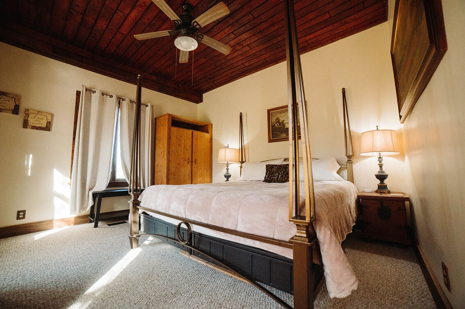 Ein Bett mit Baldachin, ein Holzschrank, ein Nachttisch mit Lampe und ein Deckenventilator in einem Zimmer mit Holzbalken.