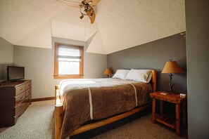 Une chambre à coucher comprenant un lit, une commode, une table de chevet, une lampe, un ventilateur de plafond et une fenêtre.