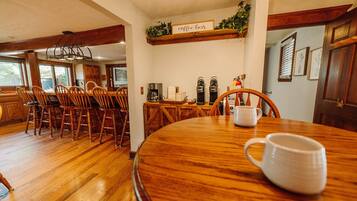 Un espace repas comprenant une table en bois, des chaises et un coin café avec deux machines à café.