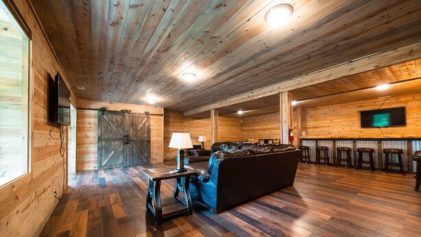 A wooden interior with a sofa, two lamps, a TV, and a bar area with stools.