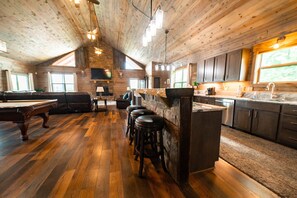 A spacious interior with a pool table, bar stools, a fireplace, and a kitchen area.