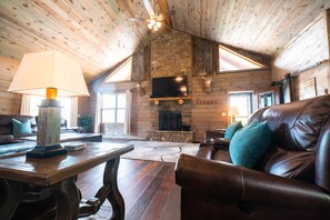 A cozy log cabin interior with a fireplace, leather sofa, and wooden flooring.