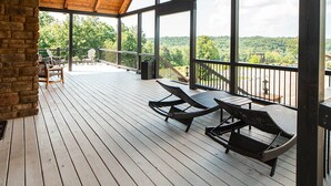 A covered outdoor deck with wooden flooring, metal railings, and a view of the landscape.