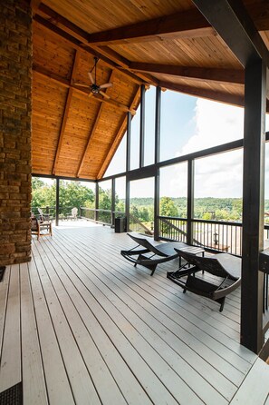 Une terrasse extérieure couverte, dotée d’un plancher en bois, de rampes en métal et offrant une vue sur le paysage.