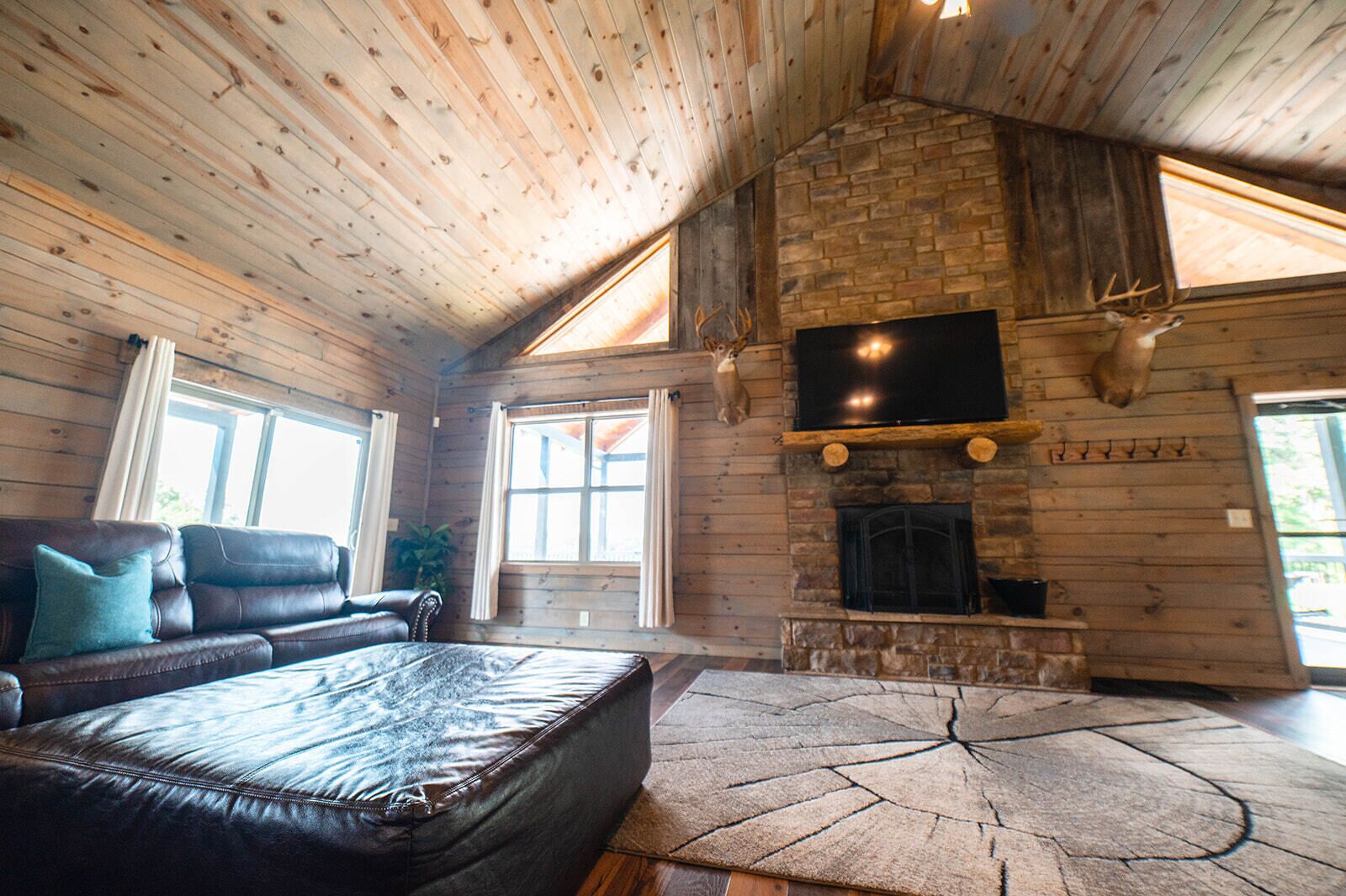 A log cabin interior with a leather sofa, a stone fireplace, and a mounted television.