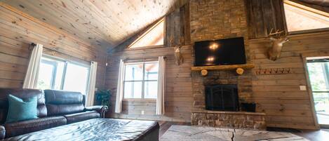 A log cabin interior with a leather sofa, a stone fireplace, and a mounted television.