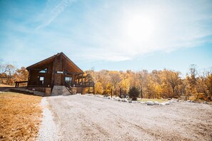 A wooden cabin with a porch and a dirt path leading to it, surrounded by autumn-colored trees.