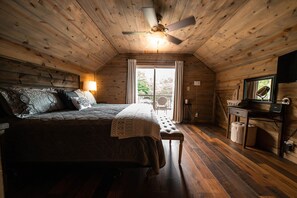 A cozy wooden cabin bedroom with a bed, bench, desk, and a ceiling fan.