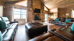 A log cabin interior with a fireplace, leather sofas, and a television.