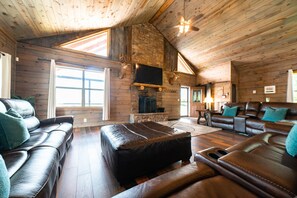L’intérieur d’une cabane en rondins, avec une cheminée, des canapés en cuir et un téléviseur.