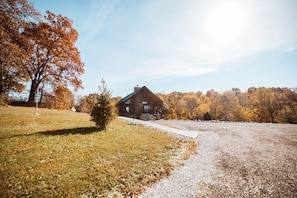 A rustic cabin with a wooden exterior, surrounded by a gravel driveway and a grassy area with a small tree.