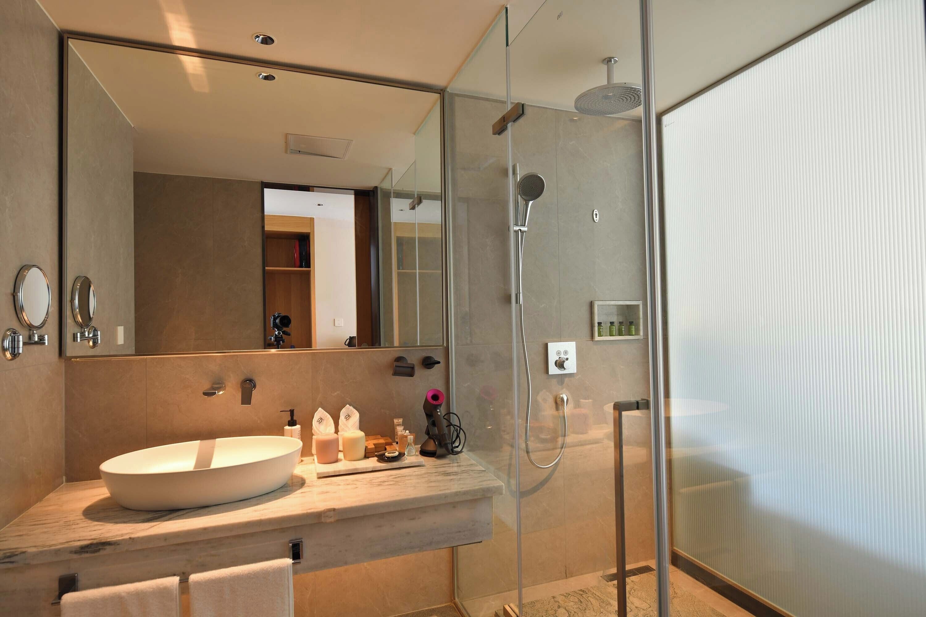 Un baño moderno con un espejo grande, un lavabo redondo y una cabina de ducha con paredes de vidrio.