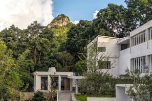 A modern building with a flat roof, surrounded by lush greenery and a prominent mountain in the background. - Zhiye Resort Hotel (Anshun)