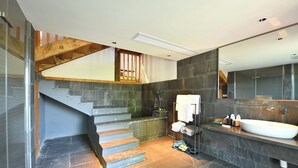 A modern bathroom with a large mirror, a white sink, and a wooden staircase.