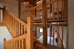 Una escalera de madera que sube a un dormitorio tipo loft con una cama y un ventanal.